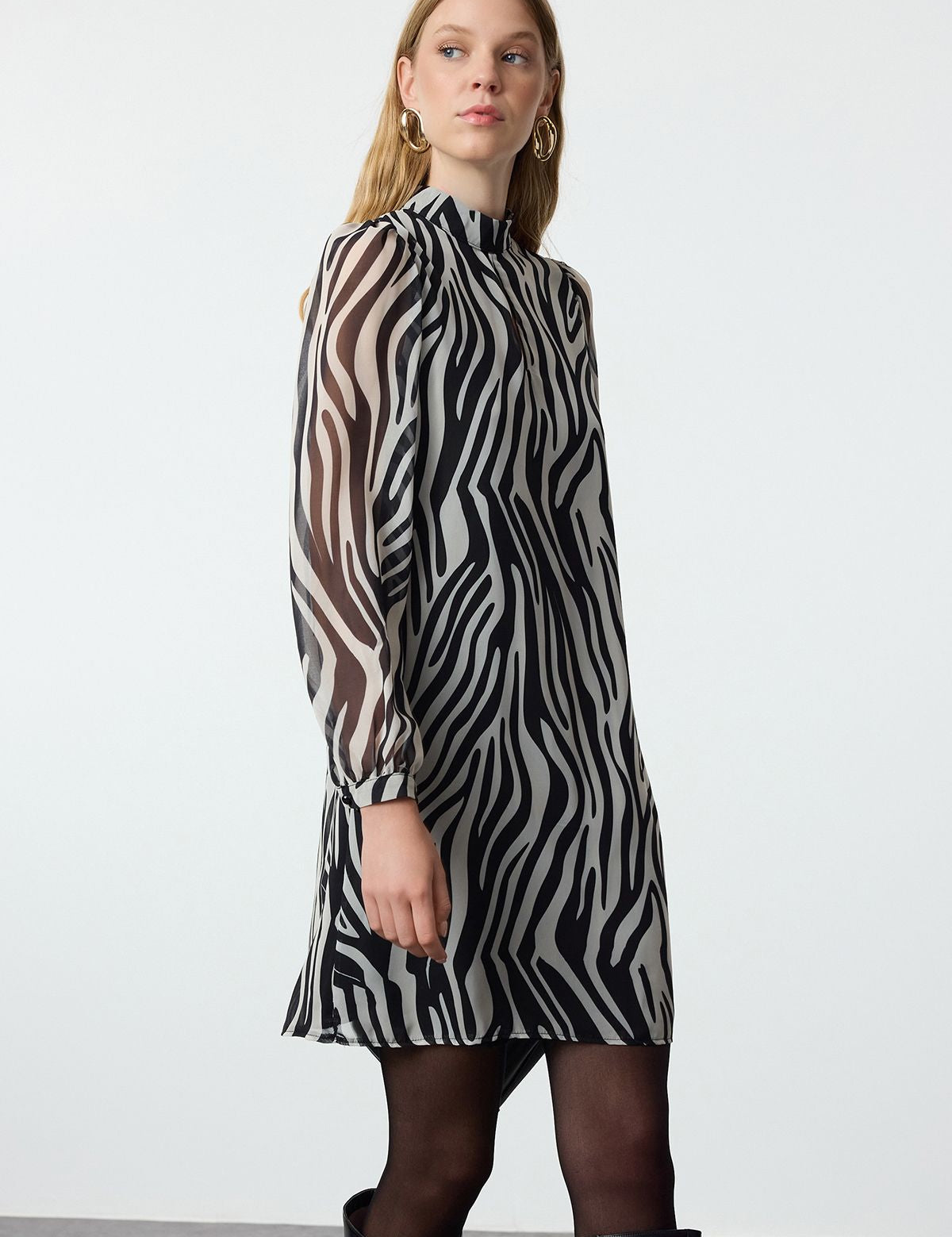 Turn heads with our Zebra Print Long Sleeve Shift Dress, featuring a bold black and white animal print, sheer sleeves, and a high neck. Perfect for day-to-night styling, this versatile dress offers a flattering fit for any occasion. Shop now for a standout look!